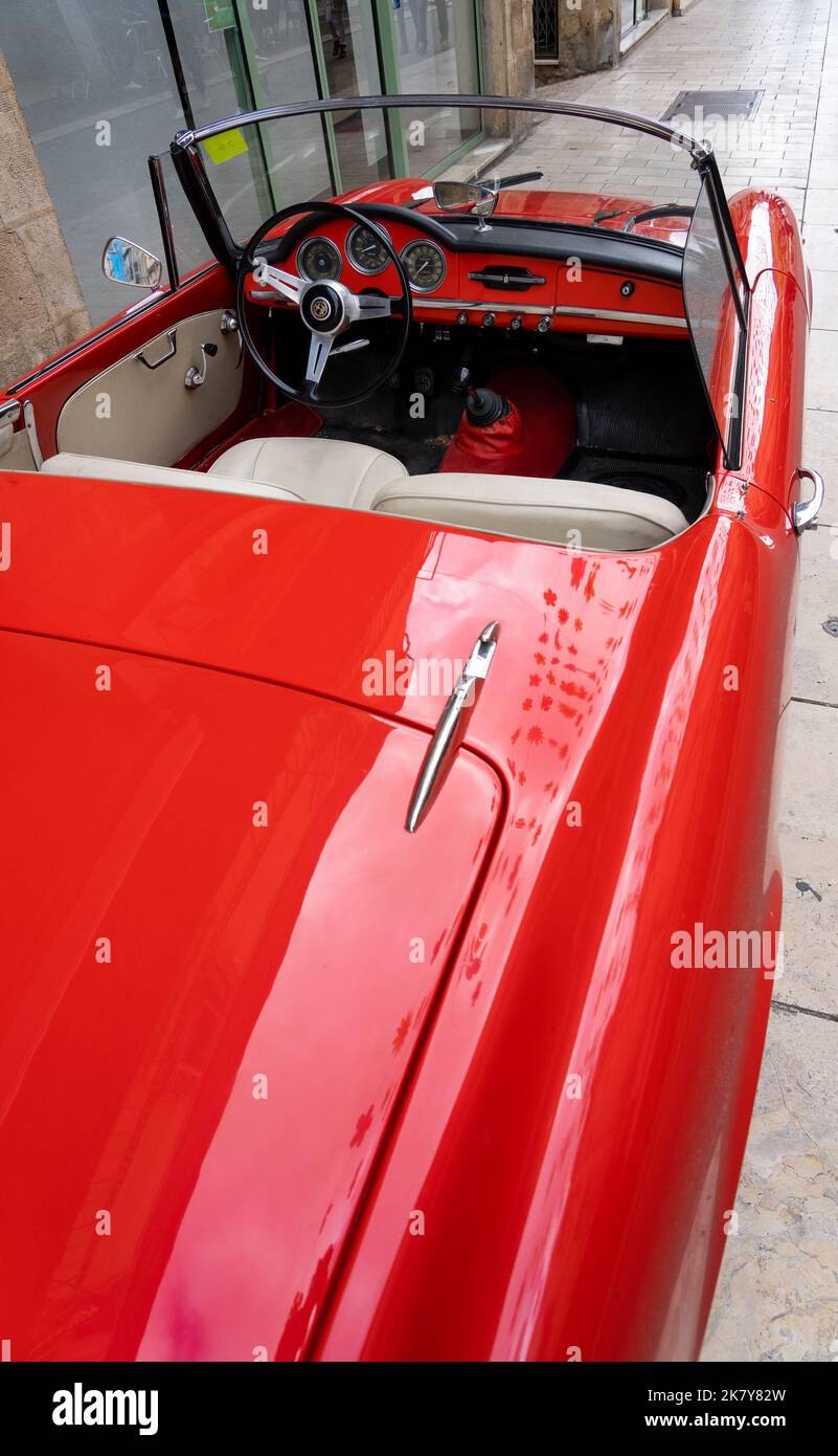 Ein klassischer Alfa Romeo 'Rosso Corsa' Spider Giula wartet auf den Eintritt zur Oldtimer- und Fahrradshow im Stadtzentrum von Sarlat-la-Caneda Stockfoto