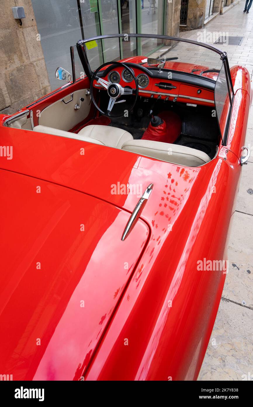 Ein klassischer Alfa Romeo 'Rosso Corsa' Spider Giula wartet auf den Eintritt zur Oldtimer- und Fahrradshow im Stadtzentrum von Sarlat-la-Caneda Stockfoto