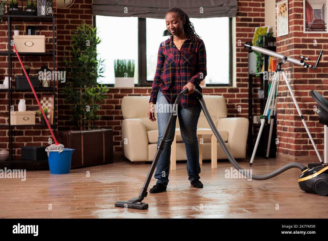 Unabhängige Frau kümmert sich um die Frühjahrsputz, saugt den Staub im Wohnzimmer Boden zu Hause. Hausfrau in Hausschuhen macht Hausarbeit mit Hingabe, säubert und reinigt den ganzen Ort. Stockfoto