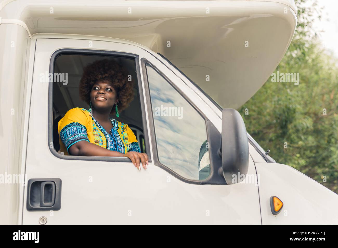 Schöne schwarze Frau in lebendigen Farben sitzt auf dem Beifahrersitz mit versteckten Fensterglas, genießen frische Luft und bewundern Sie die schöne Aussicht. Reisen und Reisen. Hochwertige Fotos Stockfoto