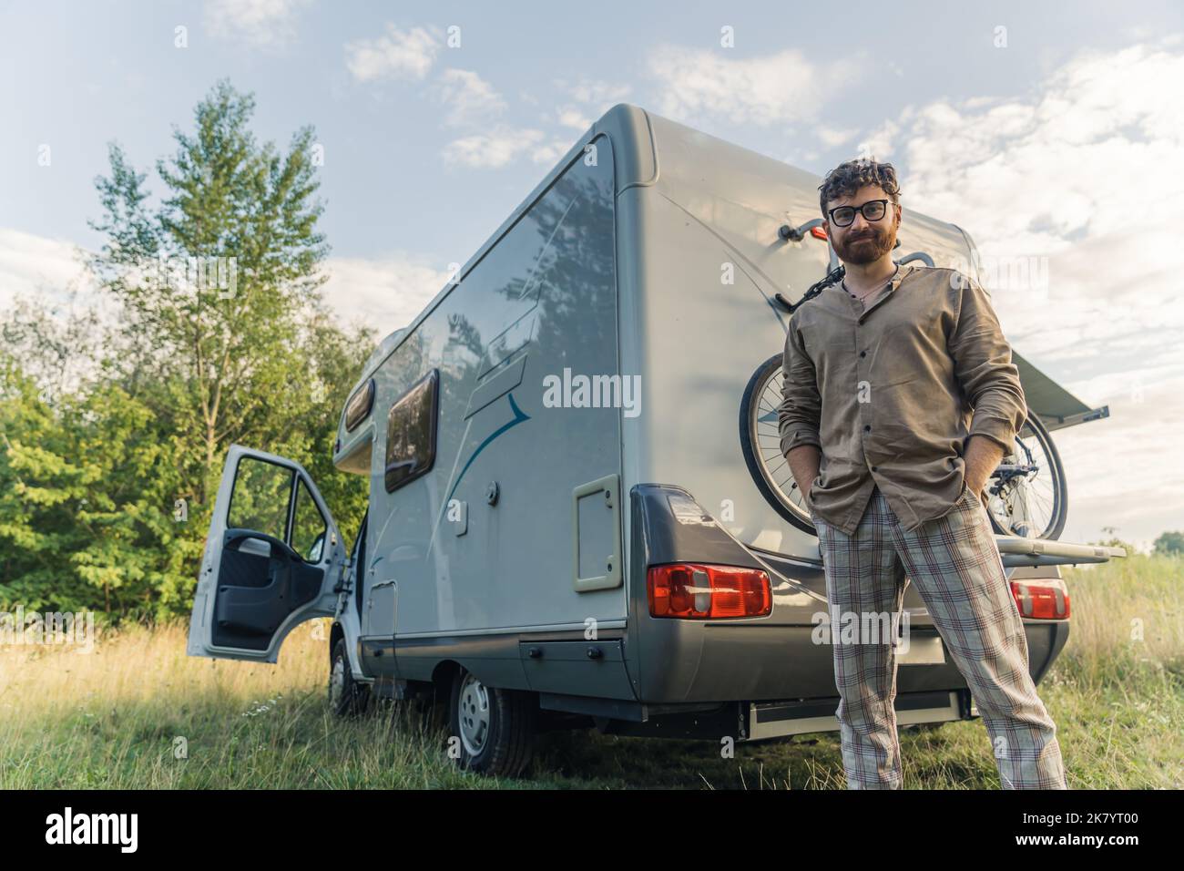 Energischer Tausendjähriger kaukasischer Hipster in beigefarbener Freizeitkleidung, der draußen in seinem modernen weißen Reisewagen steht. Radfahren und unbeschwertes Reisen im Sommer. Hochwertige Fotos Stockfoto