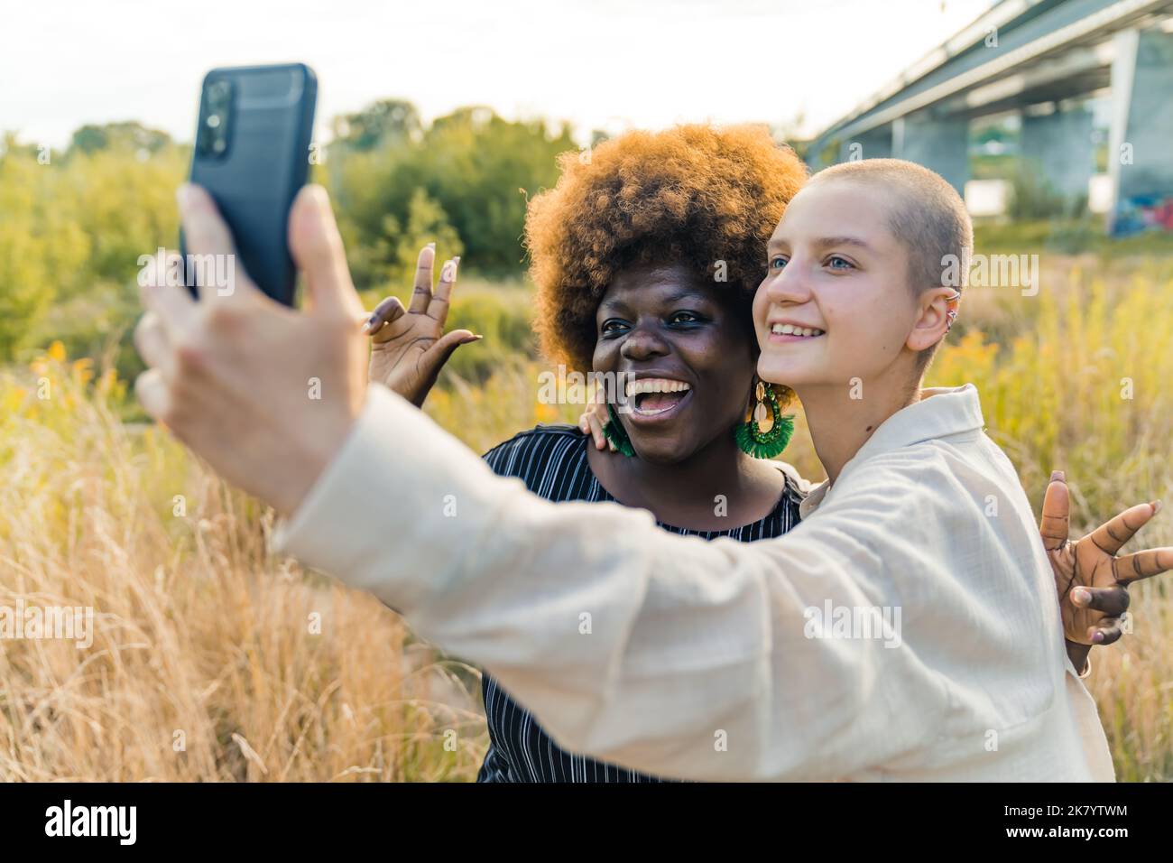 Modernes Freundschaftskonzept. Smiley schwarze Frau in ihrem späten 20s mit roter Afro-Frisur posiert für ein Selfie, das von ihren kahlköpfigen queeren kaukasischen Freunden aufgenommen wurde. Außenaufnahme. Hochwertige Fotos Stockfoto