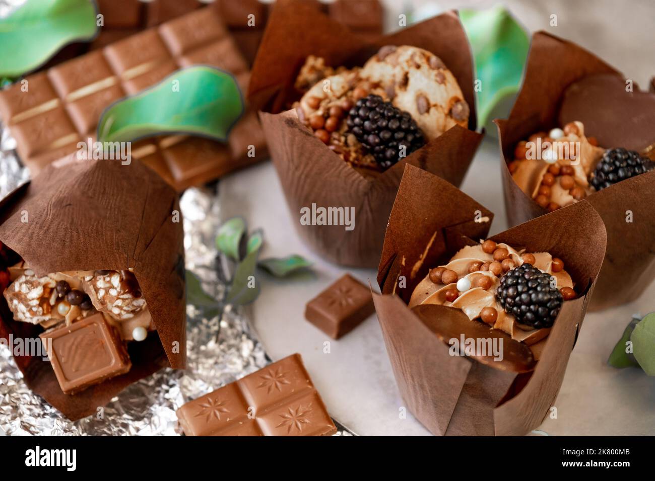 cupcake mit Brombeeren- und Eukalyptusblättern auf Silberfolie. Schokoladendessert. Verschiedene süße Tische. Süßigkeiten und Desserts. Backwaren Stockfoto