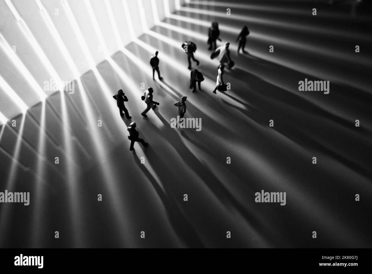 Miniaturspielzeuge Studioeinbau - Seitenansicht des Schwarz-Weiß-Effekts von Menschen mit langen Schatten, die während des Sonnenauf- oder Sonnenuntergangs auf der Straße laufen. Stockfoto