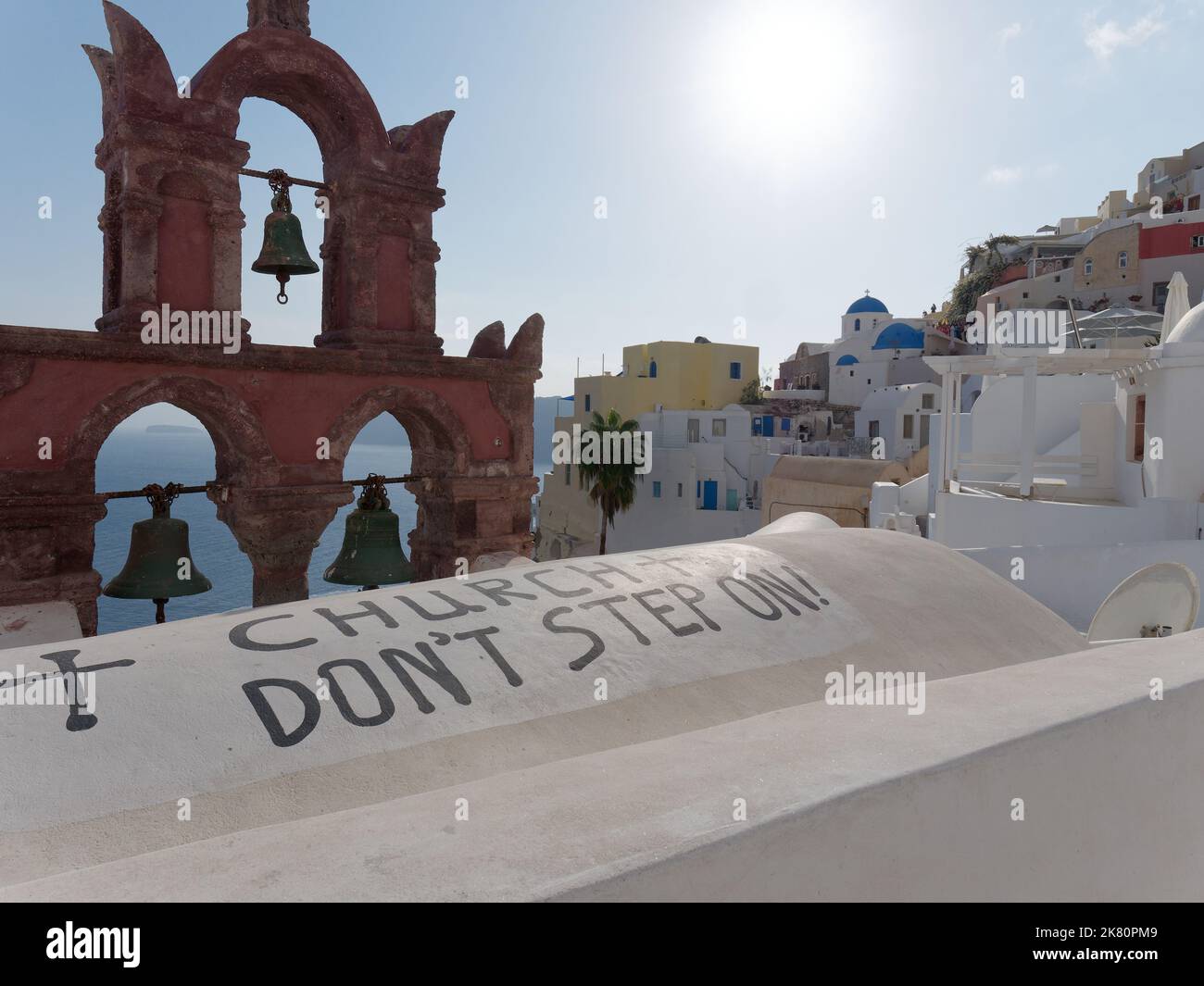 Kirchenglocken und Don t Step on Schild und blaue Kuppelkirchen in der Stadt Oia. Griechische Kykladen Insel Santorin, Griechenland. Oktober 2022. Stockfoto