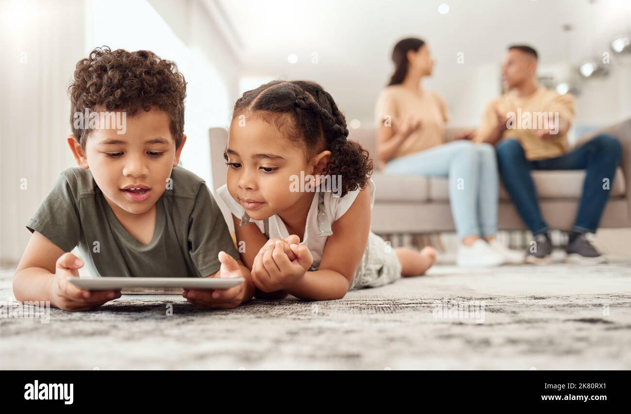 Kinder auf dem Boden mit Tablet im Wohnzimmer, sehen sich lustige und lehrreiche Videos an oder spielen mit den Eltern online auf dem Sofa. Technologie, Internet und Stockfoto