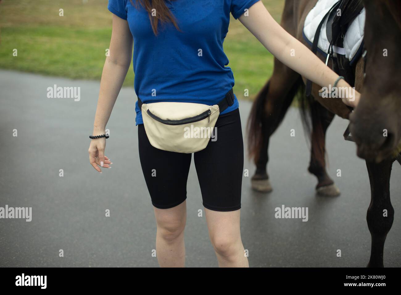 Mädchen hält Pferd. Gürteltasche. Blaues T-Shirt. Pferd halten. Junger Fahrer. Stockfoto