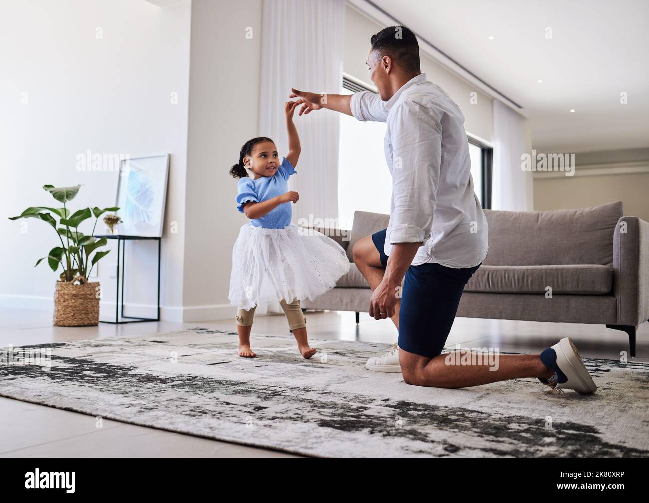 Familie, Vater und Tochter tanzen zum Spaß, zur Energie und zur Liebe im Wohnzimmer und fühlen sich glücklich, die Hände zu halten, um zu Hause zu tanzen. Mann oder Vater und Mädchen Stockfoto