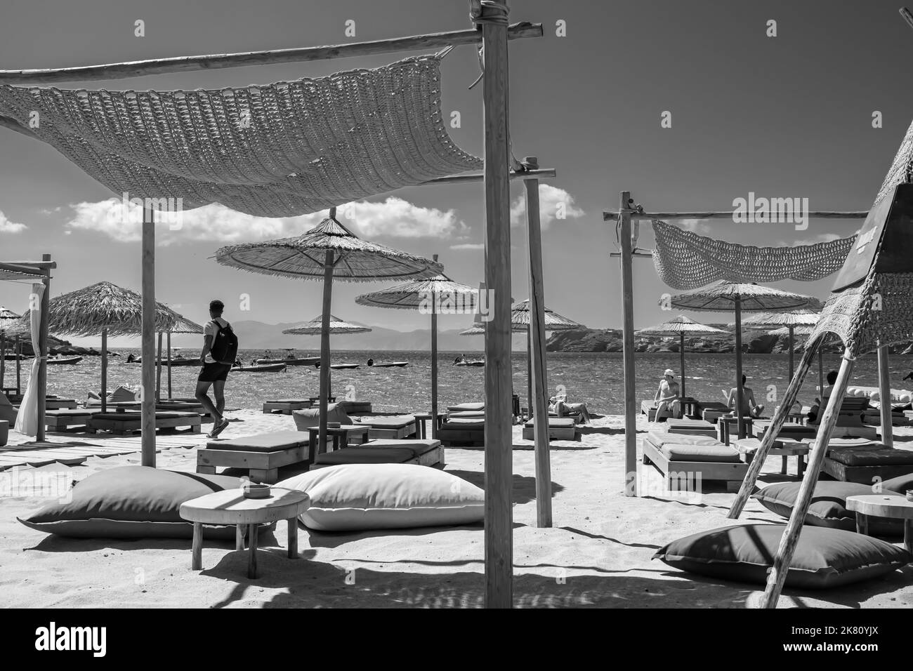 IOS, Griechenland - 6. September 2022 : Touristen entspannen sich auf luxuriösen Holzliegen am berühmten Strand von Mylopotas in iOS Griechenland in Schwarz und Weiß Stockfoto