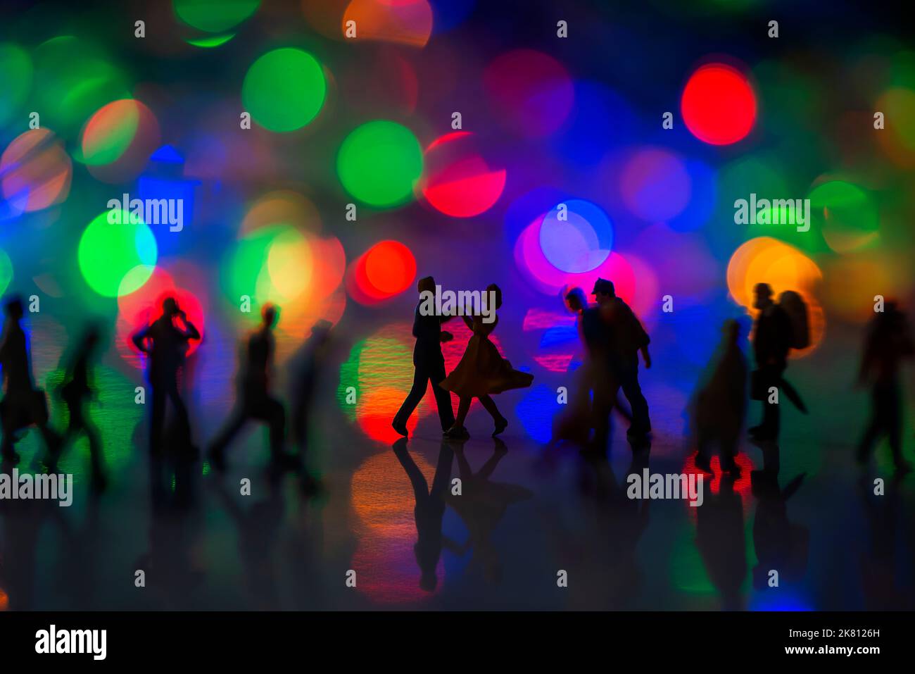 Miniatur-Spielzeug für Menschen - Ein Paar, das gemeinsam auf der Straße unter geschäftigen Pendlern tanzt, mit bunten Bokeh-Lichtern und Glücksgedanken. Stockfoto