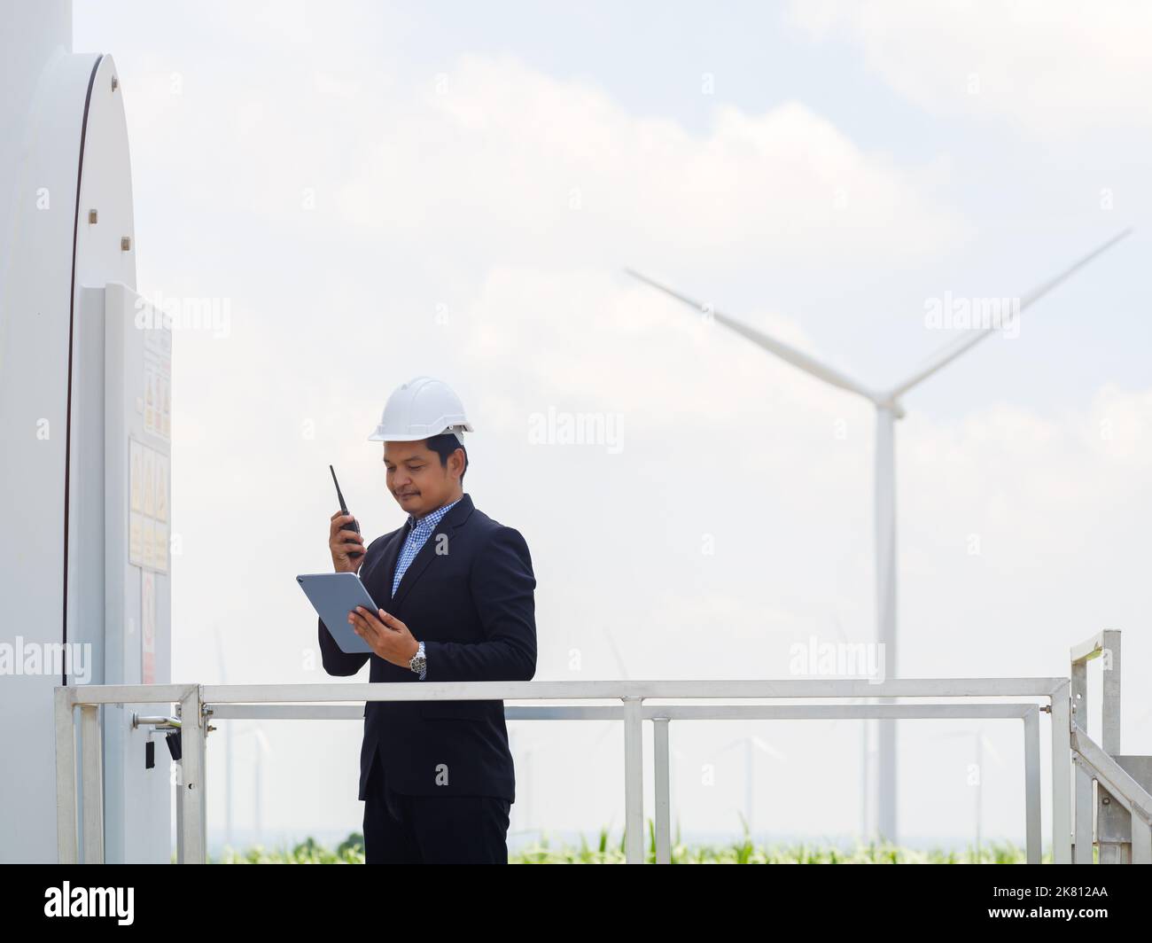 Der Ingenieur-Manager in einem Anzug steuert und überwacht den Betrieb einer Windenergieanlage im elektrischen Kontrollraum mit einem Tablet.Konzept der Windschaufeln Stockfoto