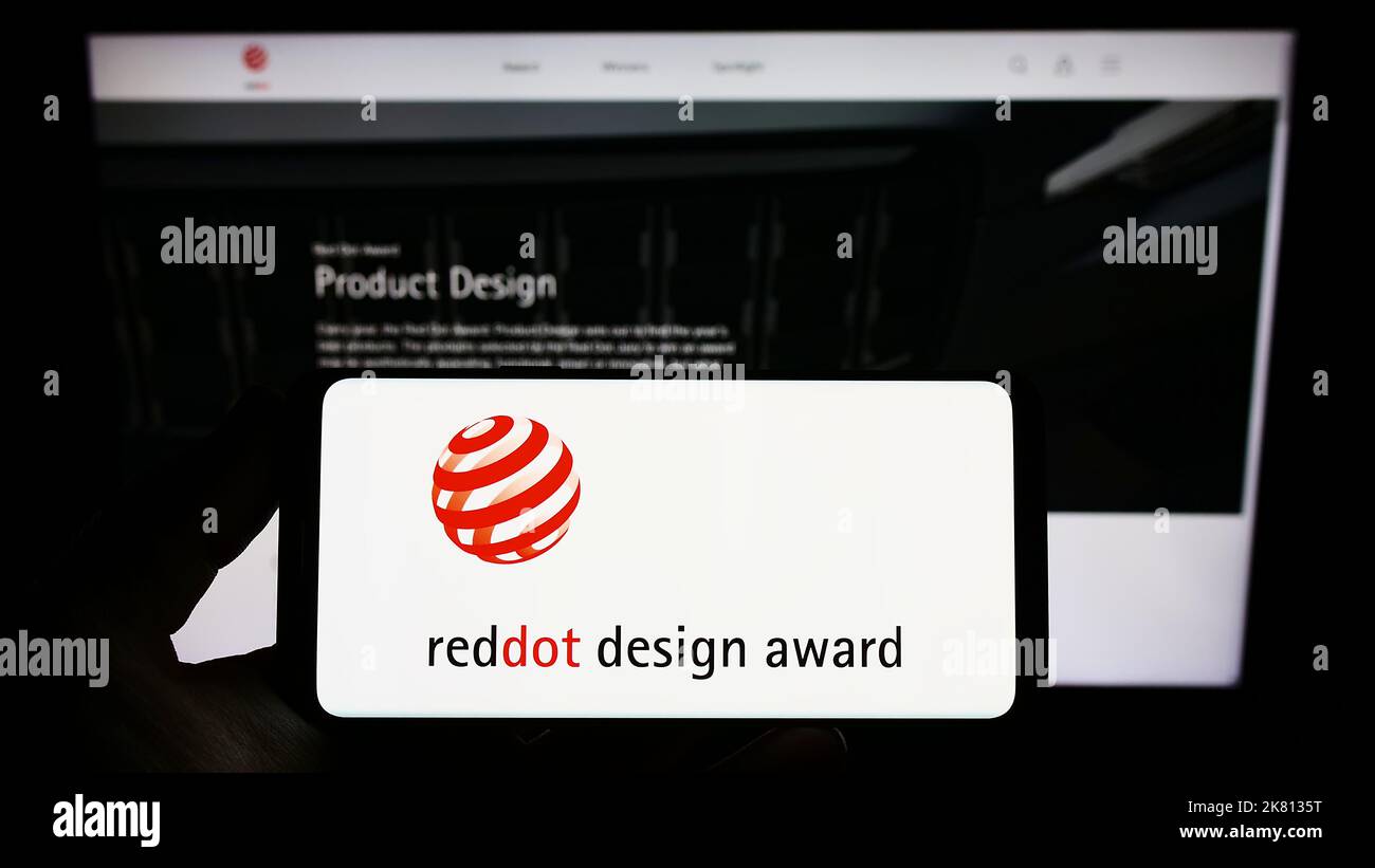 Person, die Smartphone mit Logo des deutschen internationalen Preises Red Dot Design Award auf dem Bildschirm vor der Website hält. Konzentrieren Sie sich auf die Telefonanzeige. Stockfoto