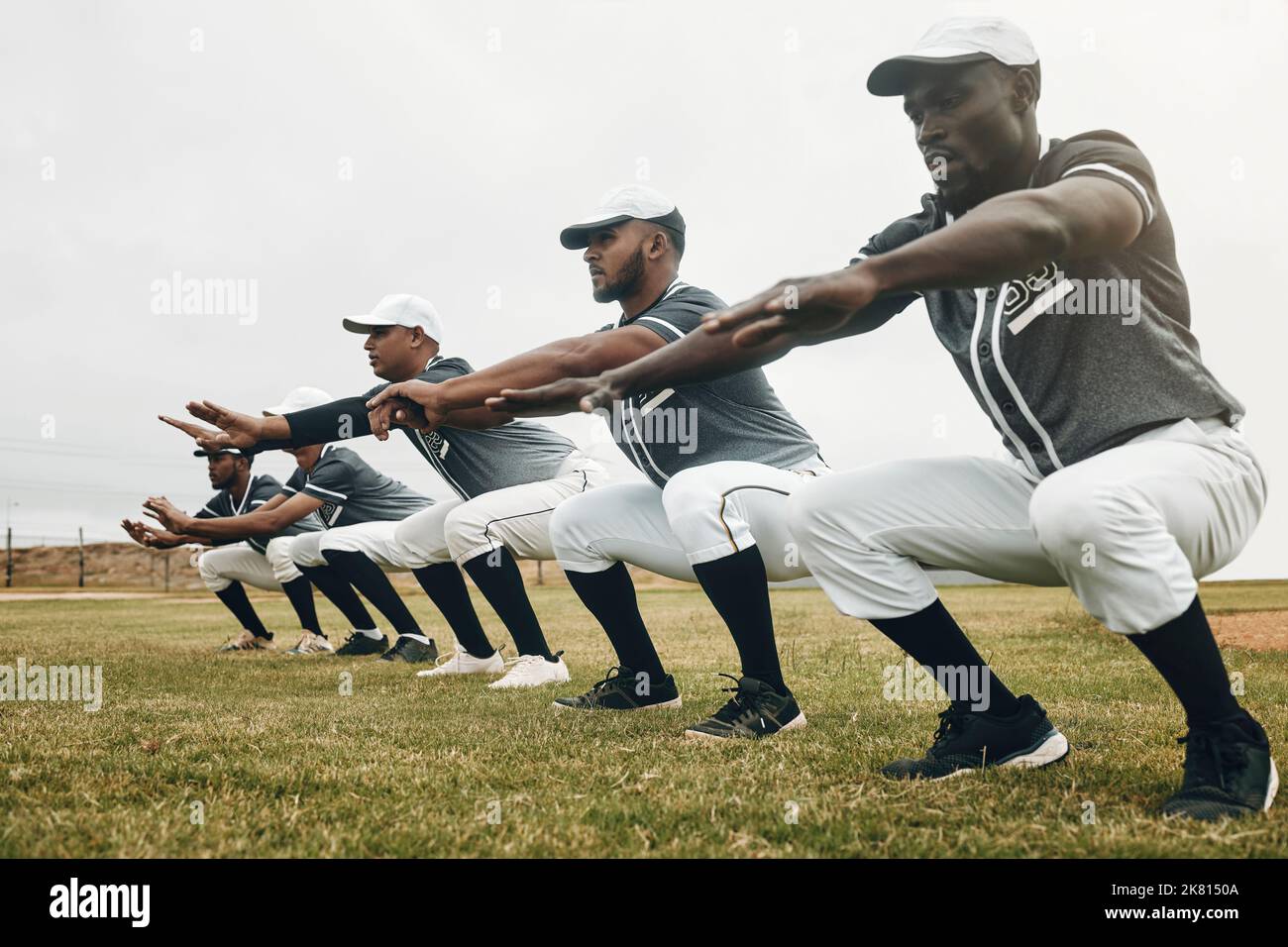 Team-, Stretching- und Baseballspieler für Spiel, Bewegung und Baseballspiele in Sportbekleidung auf dem Spielfeld. Workout, Squat und Gruppe für Match vorbereiten, Wellness und Stockfoto