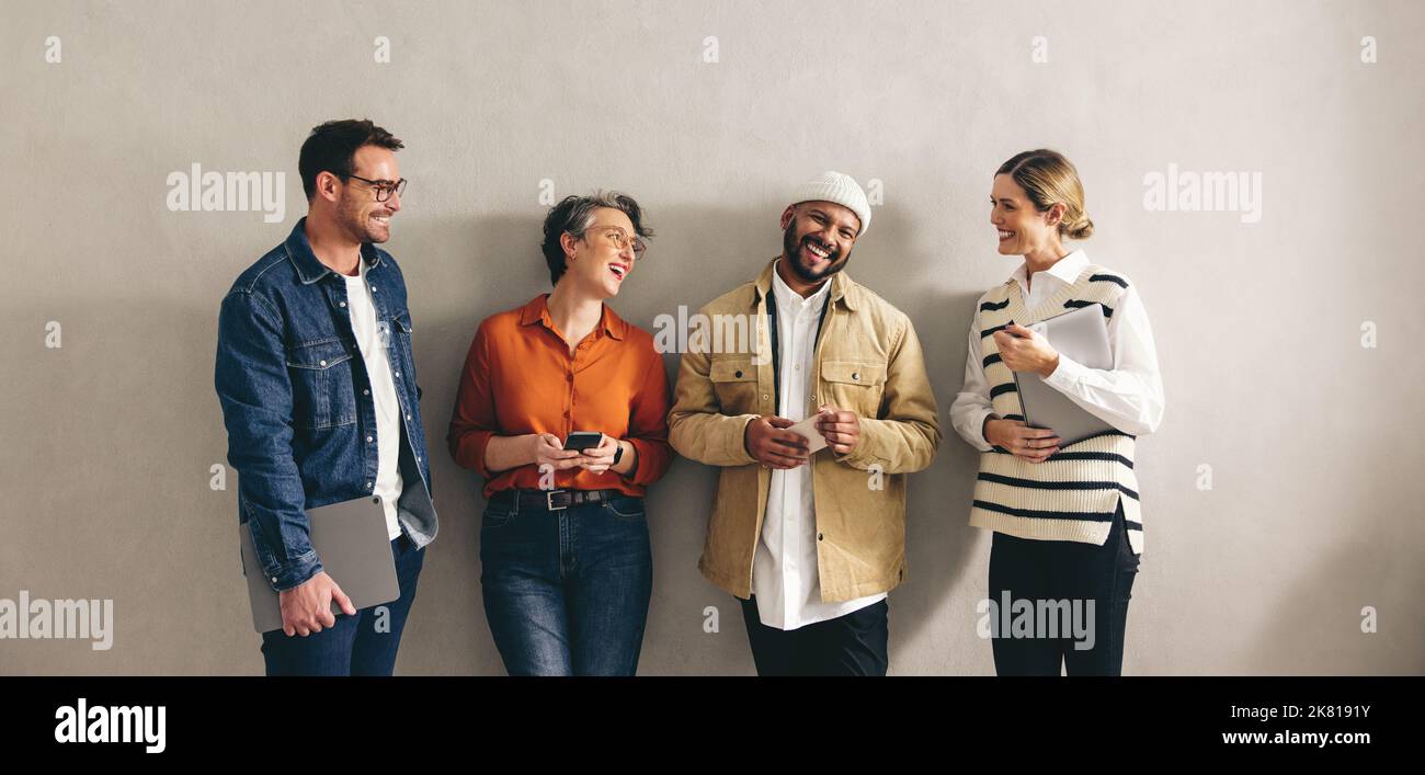 Eine Gruppe glücklicher Geschäftsleute, die fröhlich lächeln und auf ein Interview warten. Kandidaten in der engeren Auswahl mit verschiedenen digitalen Geräten Stockfoto