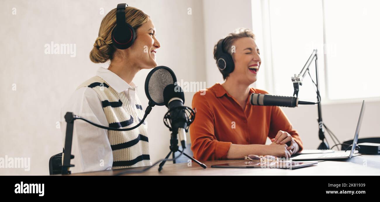Podcast und Spaß. Weibliche Podcasterinnen lachen fröhlich, während sie eine Audioübertragung in einem Studio mithosten. Zwei glückliche Frauen, die einen Internet-Podcast aufzeichneten Stockfoto