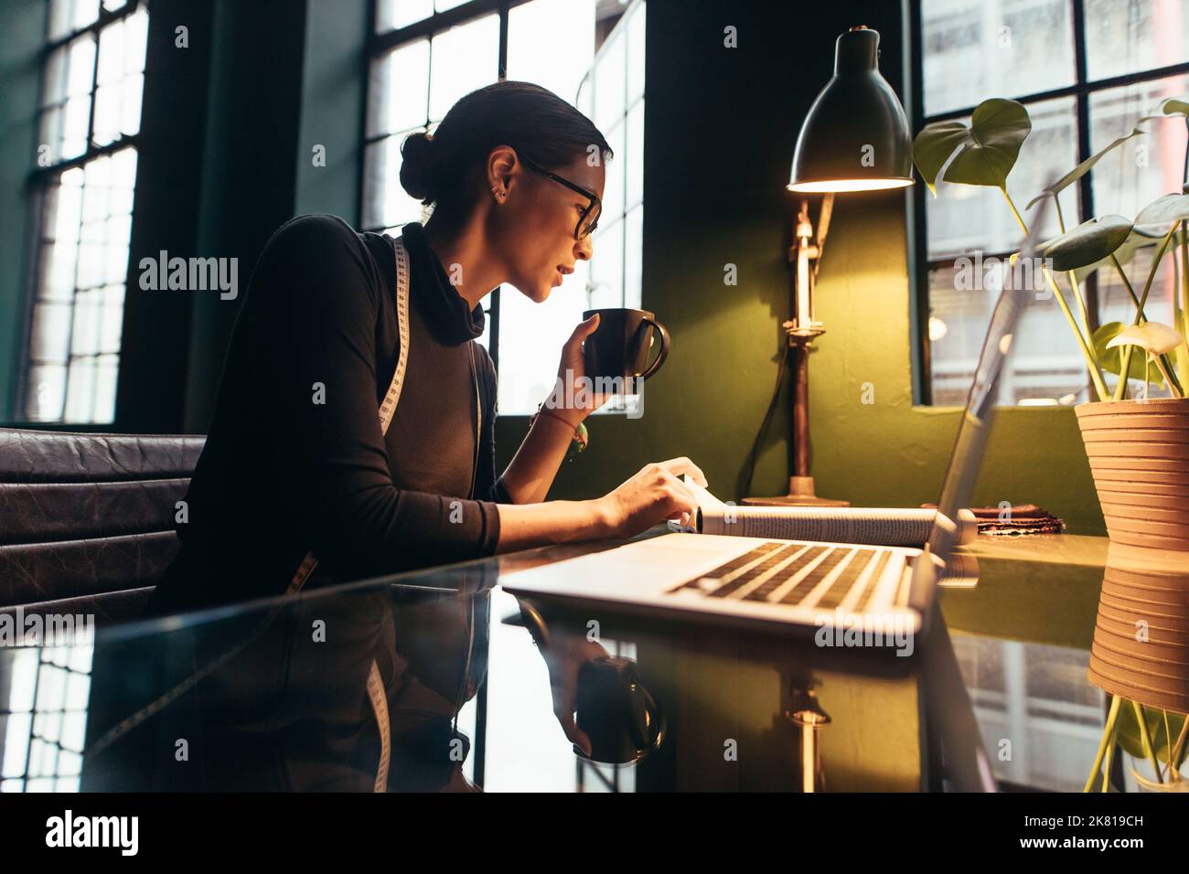 Modedesignerin liest Buch und trinkt Kaffee. Asiatische Frau beschäftigt an ihrem Schreibtisch arbeiten. Stockfoto