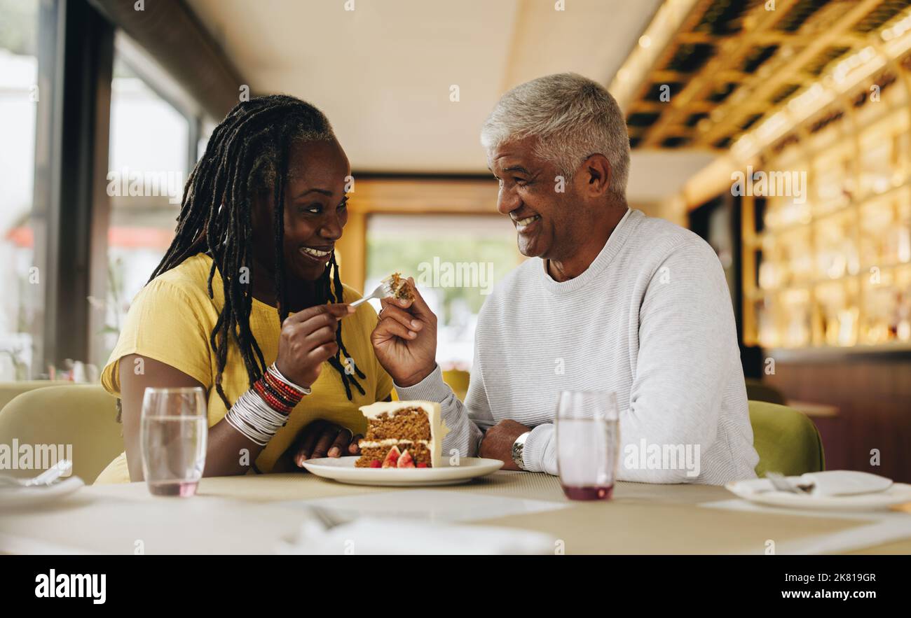 Glückliches Seniorenpaar lächelt sich gegenseitig an, während es einen leckeren Kuchen in einem Café teilt. Sorgenfreies Seniorenpaar, das eine gute Zeit in einem Restaurant hat. Reif Stockfoto