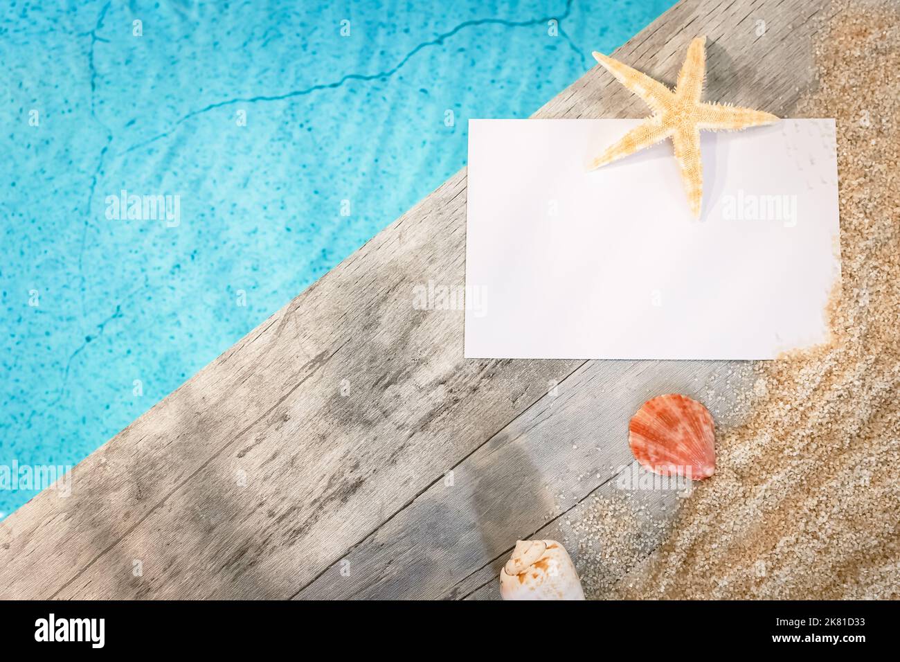 Einladungskarte ohne Inschrift von oben gesehen auf einem Holzpflaster über einem Pool mit Seesternen. Atmosphärenurlaub im Sommer. Stockfoto