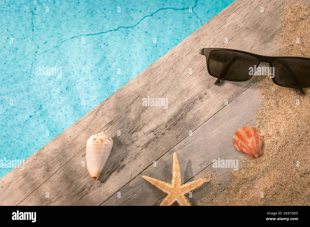 Sonnenbrillen von oben auf einem Holzpflaster über einem Pool mit einem Seesternen. Ambiance Urlaub im Sommer. Stockfoto