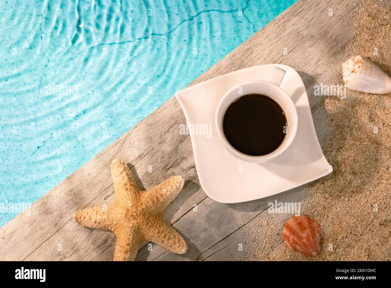 Kaffeetasse von oben auf einem Holzpflaster über einem Pool mit Seesternen. Ambiance Urlaub im Sommer. Stockfoto