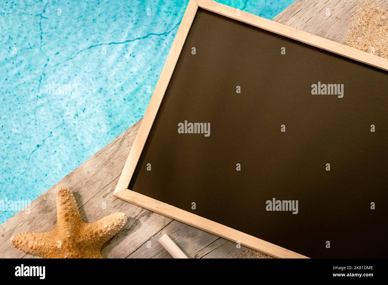 Schiefermalerei ohne Inschrift von oben auf einem Holzpflaster über einem Pool mit Seesternen. Atmosphärenurlaub im Sommer. Stockfoto