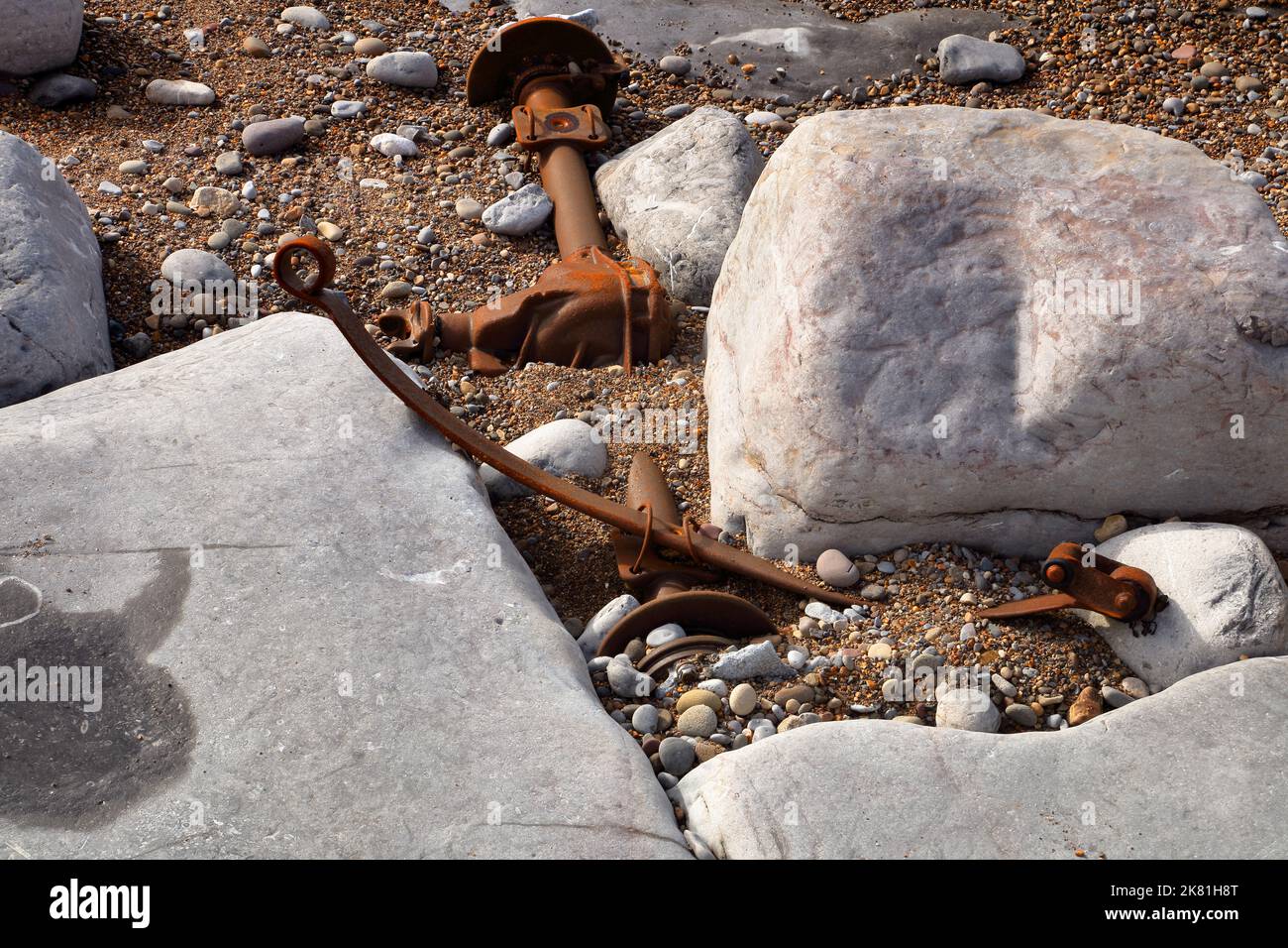 Zertrümmerte und zerbrochene Hinterachse, die zwischen Felsen festsitzt und teilweise in einer kleinen Bucht entlang der Küste vergraben ist. Stockfoto