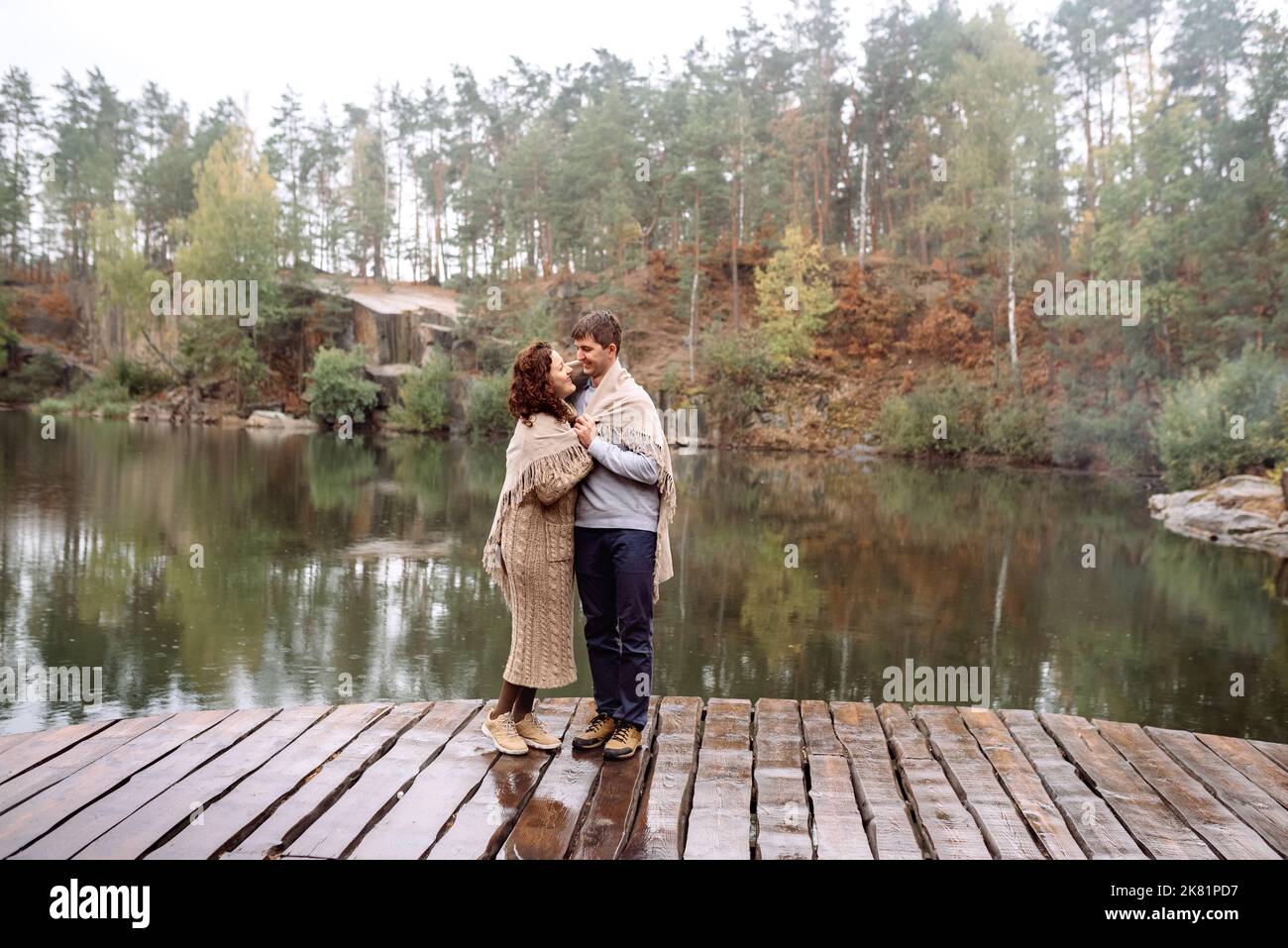 Glückliches Paar reist im Herbst an einem malerischen Ort zwischen Felsen und Wasser. Bedeckt mit einer Regendecke. Soft Focus .Ukraine, Korostyschiv Steinbruch. Stockfoto