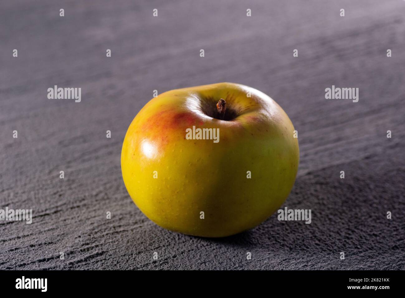 Ein gelb-rot reifer Apfel auf grauem Betongrund, selektiver Fokus, Nahaufnahme, Draufsicht. Diät-Food-Konzept. Stockfoto