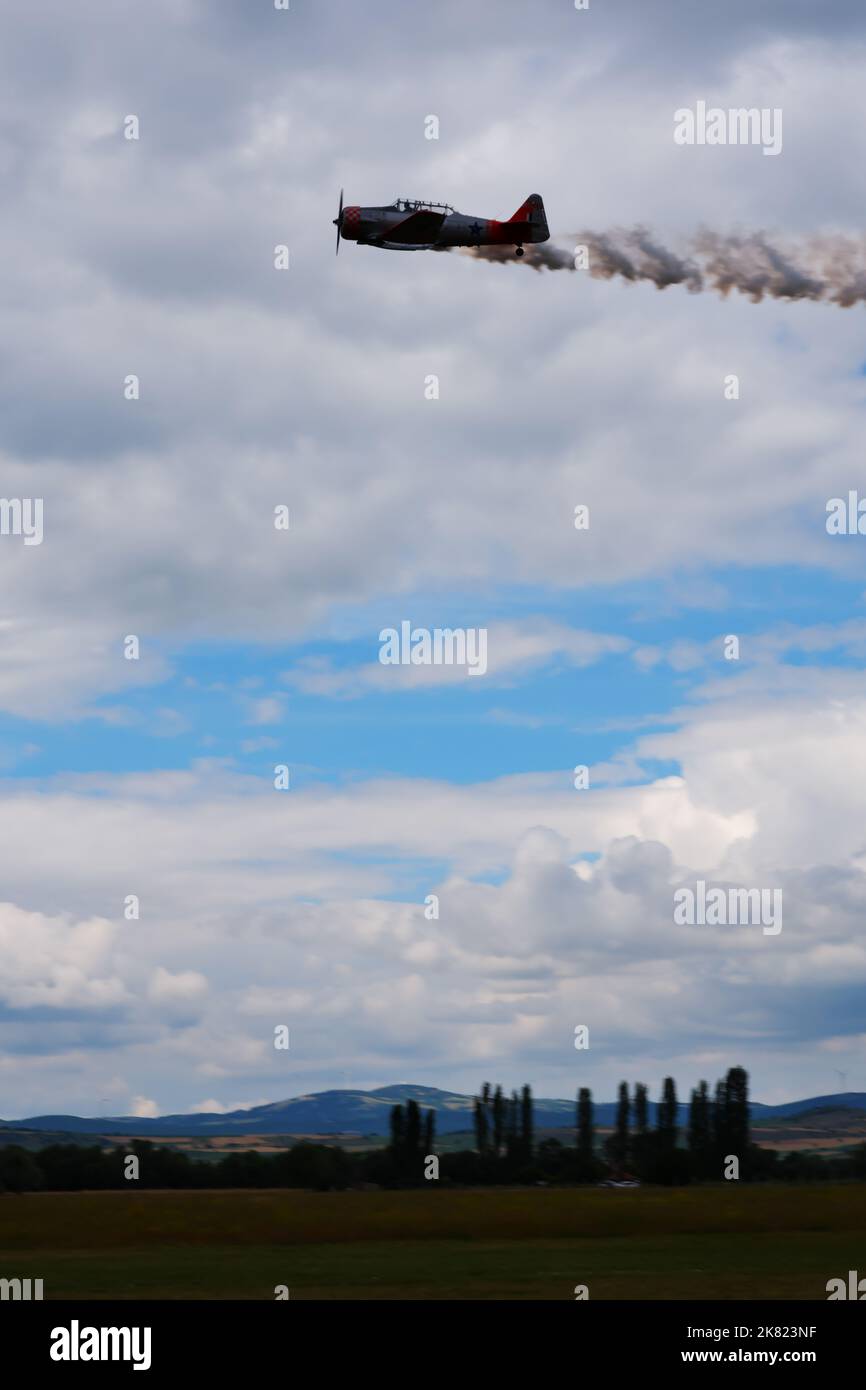 Kleines Flugzeug, das dicht am Boden fliegt, mit Rauch im Hintergrund Stockfoto