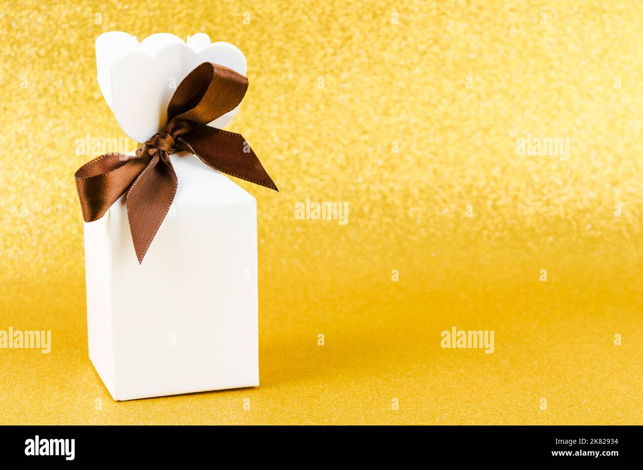 Geschenkbox mit braunem Band auf goldenem Glitzer-Struktur-weihnachtshintergrund. Stockfoto