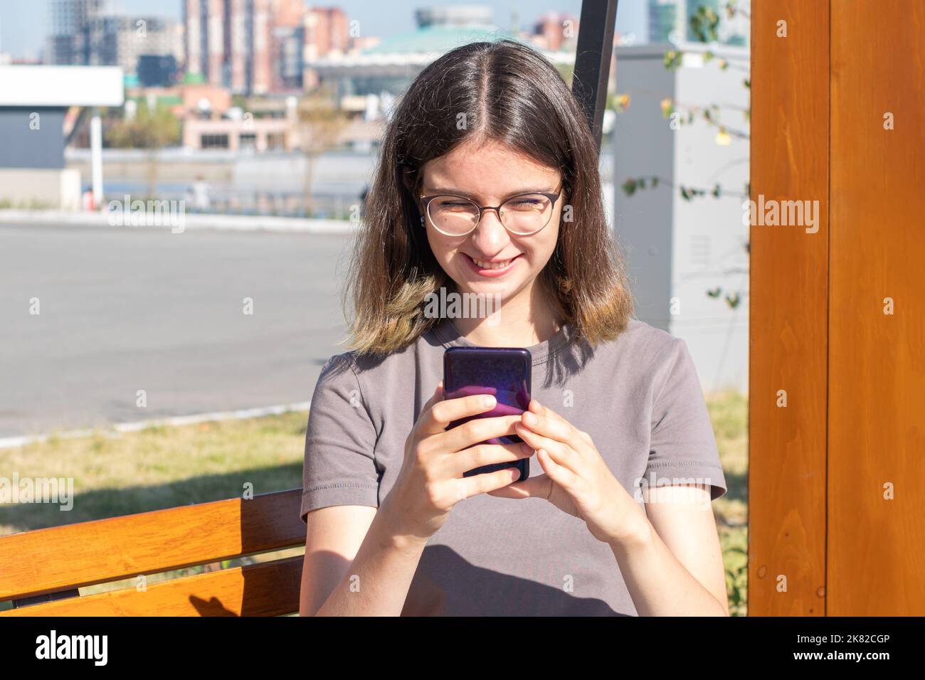 Eine spanische Studentin mit Brille, die SMS auf ein Mobiltelefon schreibt, im Internet nach etwas sucht und online mit Freunden kommuniziert, die draußen sitzen Stockfoto