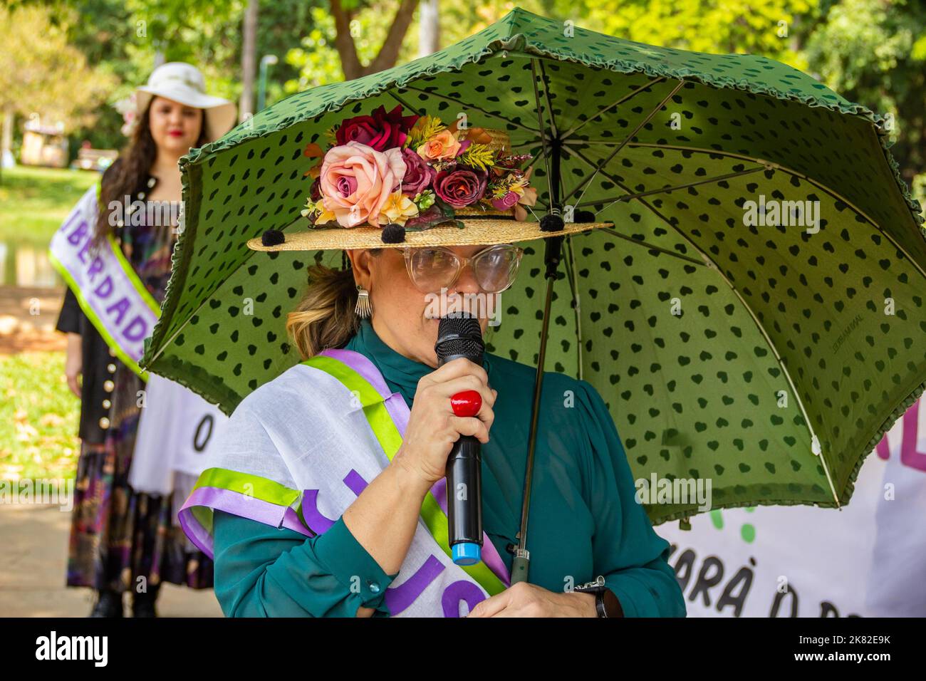 Goiânia, Goias, Brasilien – 12. Oktober 2022: Eine Frau, gekleidet als Suffragette, spricht während einer Handlung in das Mikrofon und hält einen Regenschirm. Stockfoto