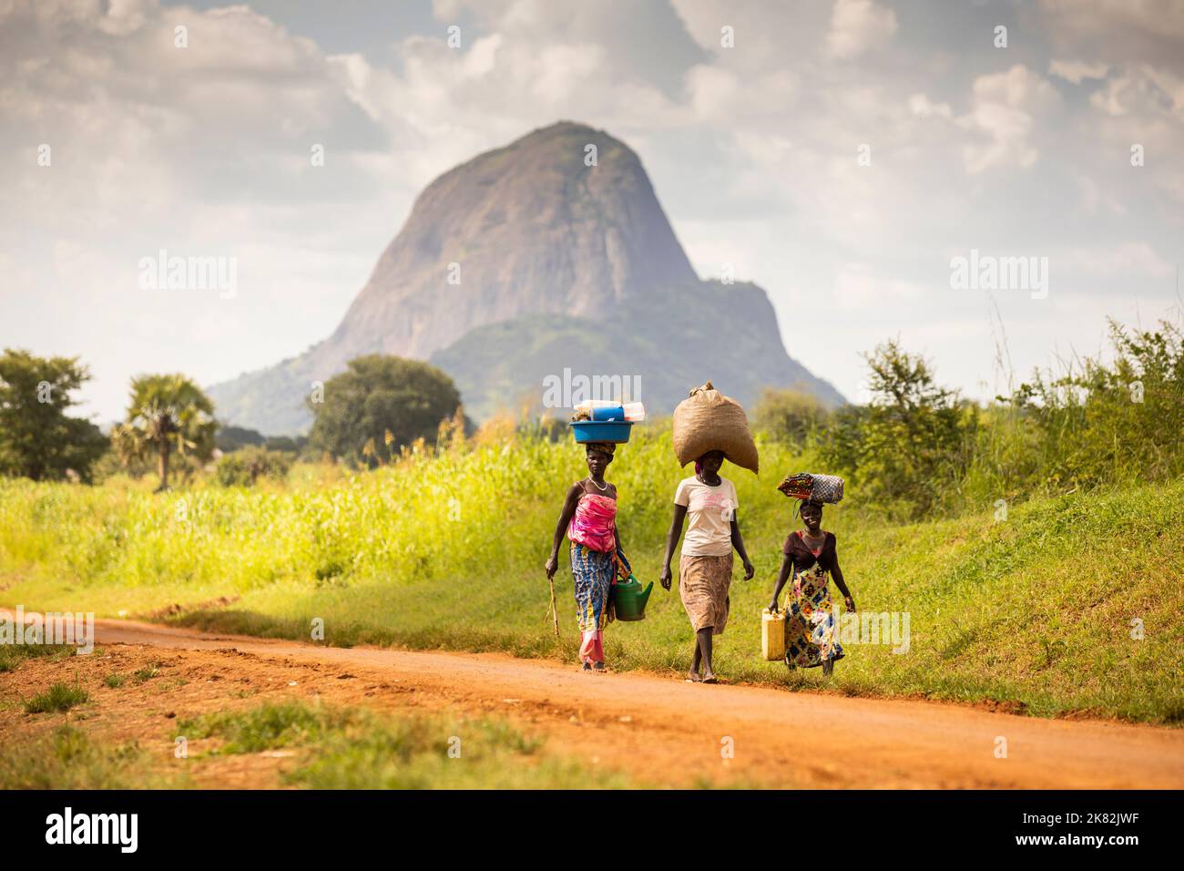 Frauen gehen gemeinsam eine abgelegene Straße entlang unter einer dramatischen Bergkulisse in Uganda, Ostafrika. Stockfoto