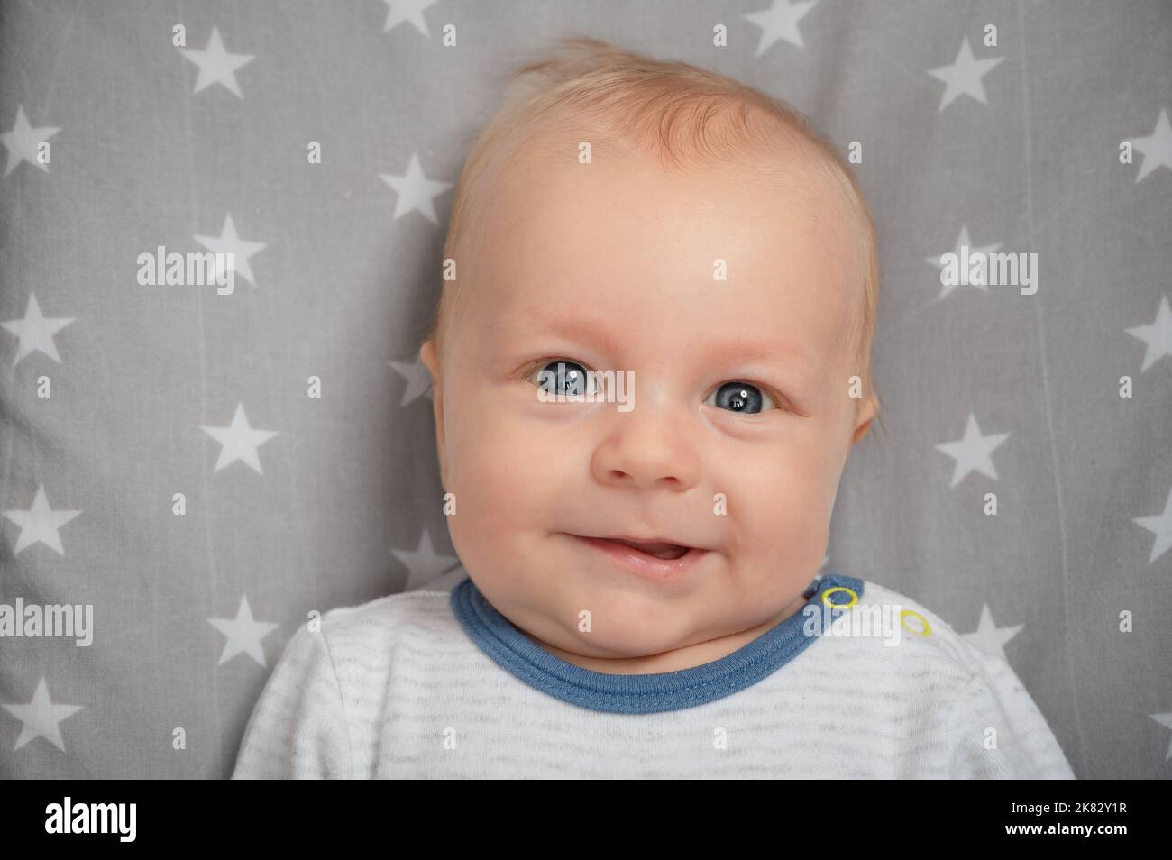 Porträt eines lächelnden Neugeborenen mit offenem Mund, Nahaufnahme. Glücklich lächelndes Kind mit blauen Augen, Blick auf die Kamera. Gesichtsausdruck. Stockfoto