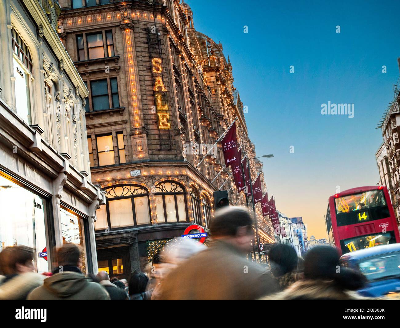 VERKAUFSSCHAREN HARRODS SALE SCHILD Harrods Kaufhaus in der Abenddämmerung mit beleuchteten 'Sale' Schild und Massen von Käufern Taxi und roten Bus Knightsbridge London SW1 Stockfoto