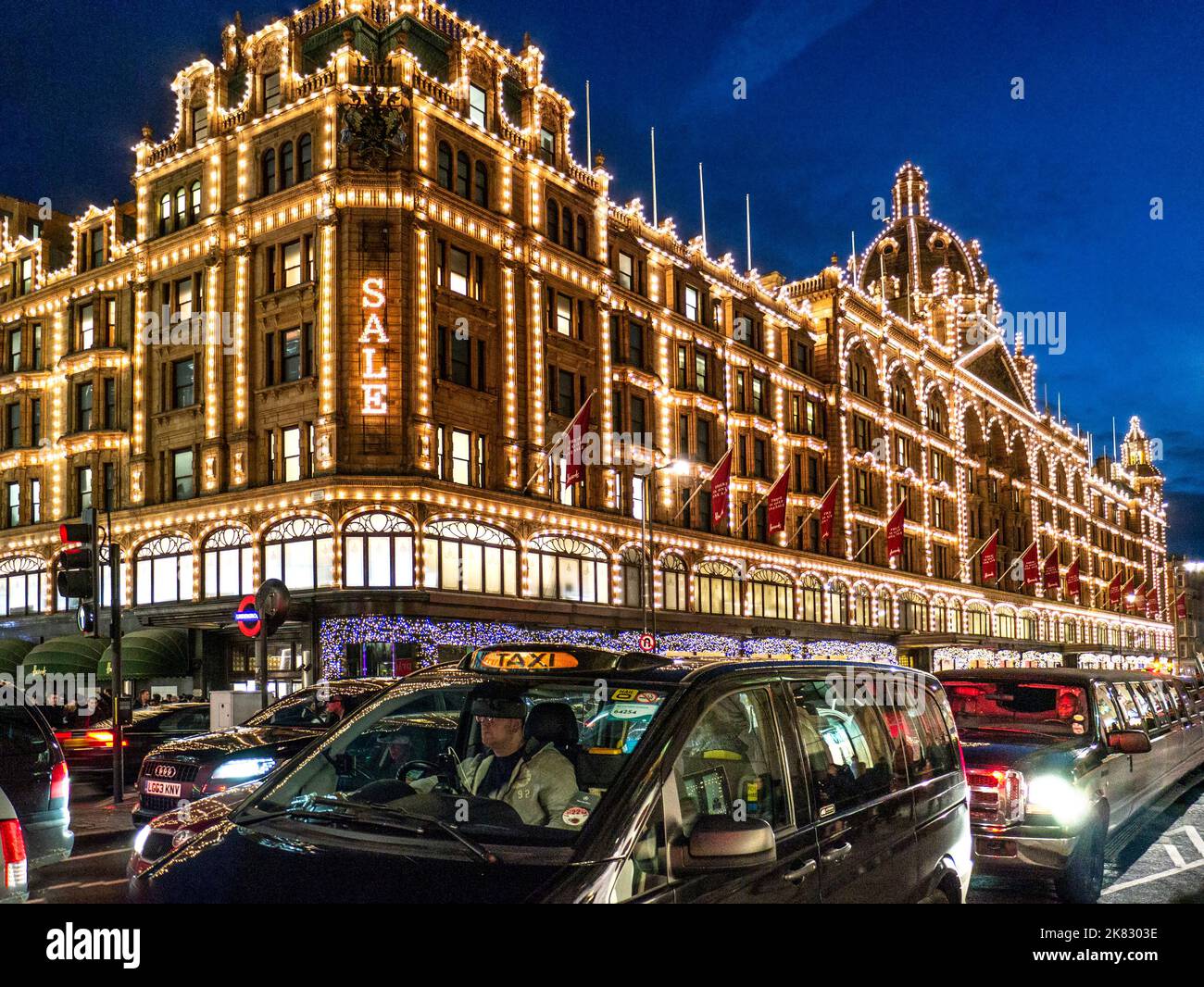 VERKAUF Harrods Kaufhaus in der Abenddämmerung mit Verkaufsschild Käufer und vorbei an Taxis Knightsbridge London SW1 Stockfoto