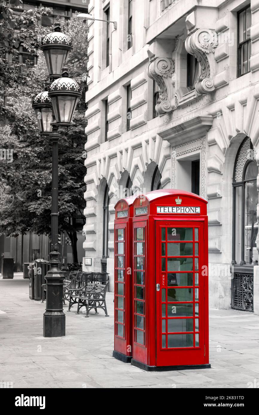 Leuchtend rote Londoner Telefonzellen auf einer Stadtstraße mit Laternenpfosten, Bänken und Bäumen im Hintergrund. Schwarz und weiß mit den Telefonzellen ausgewählt o Stockfoto