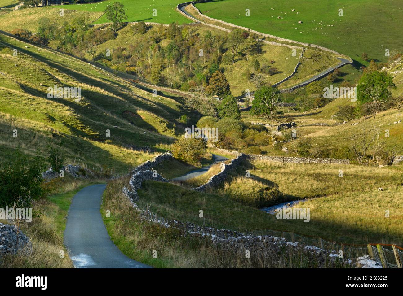 Ruhige, gewellte Landstraße (Talseiten, malerische sonnenbeschienenen Landschaften, steiler Aufstieg, Bach) - in der Nähe von Kettlewell, Yorkshire Dales, England, Großbritannien. Stockfoto