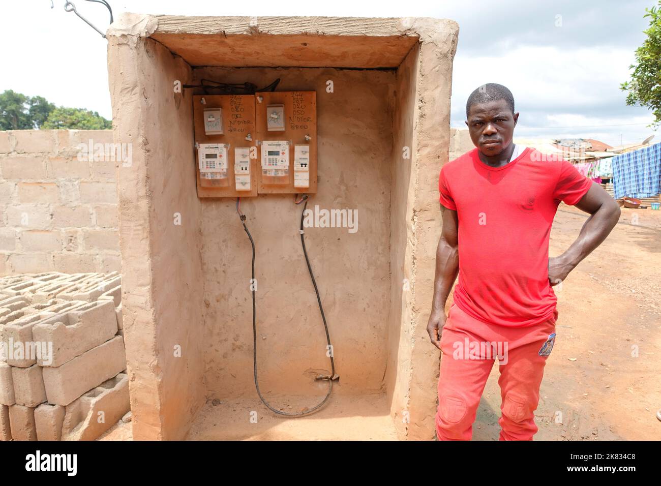Ein Bewohner posiert neben seinem neuen Stromzähler in einem armen ländlichen Dorf in der Elfenbeinküste Stockfoto
