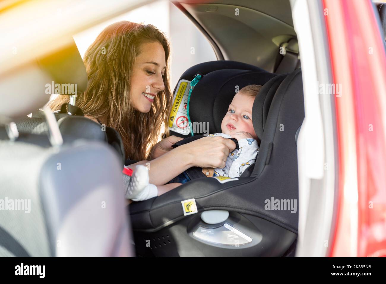 Mutter schnallt ihren Sohn auf den Autositz und legt seinen Sicherheitsgurt an Stockfoto
