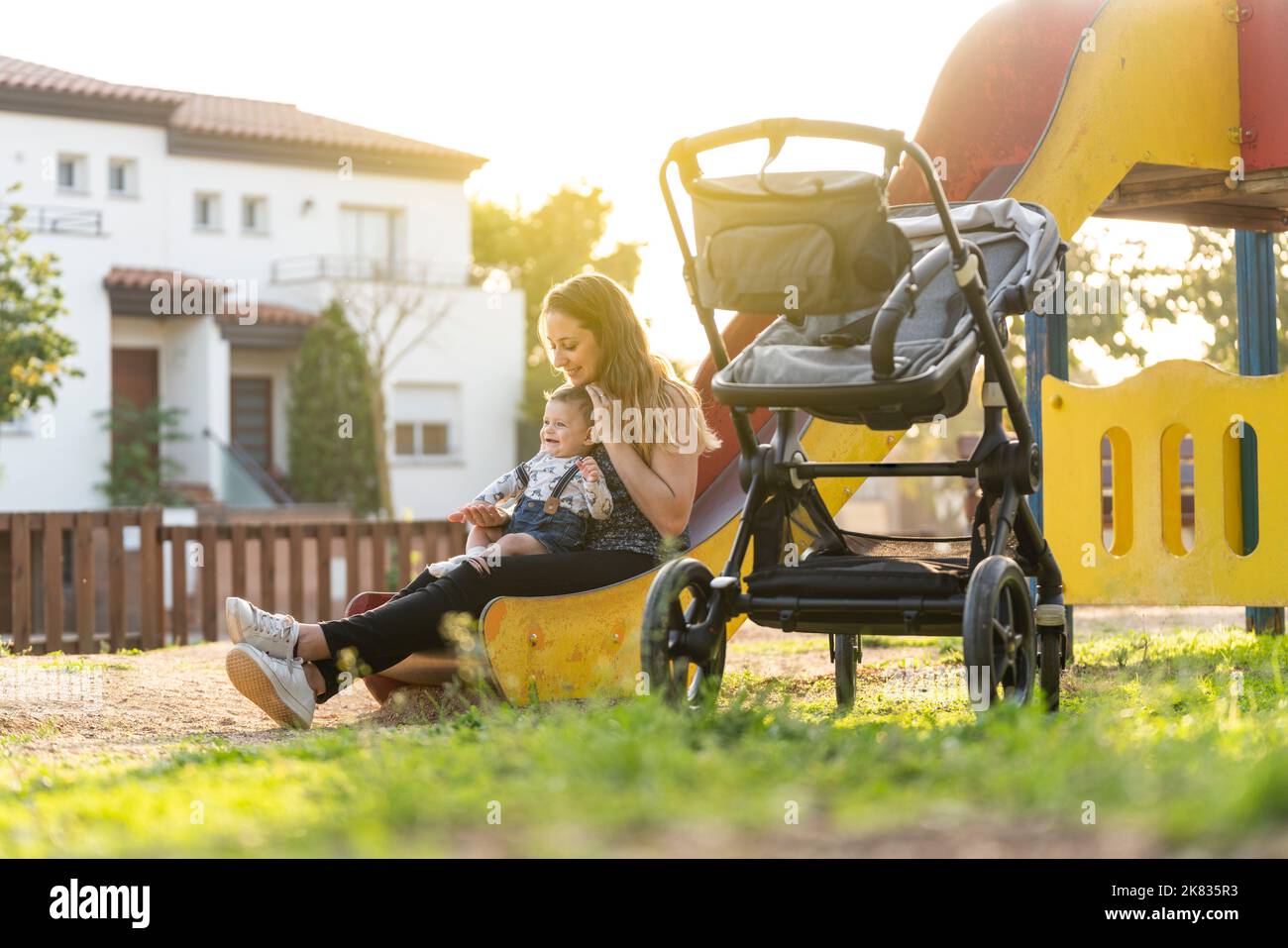 Mutter mit ihrem Baby auf einer Parkrutsche, als die Sonne untergeht Stockfoto