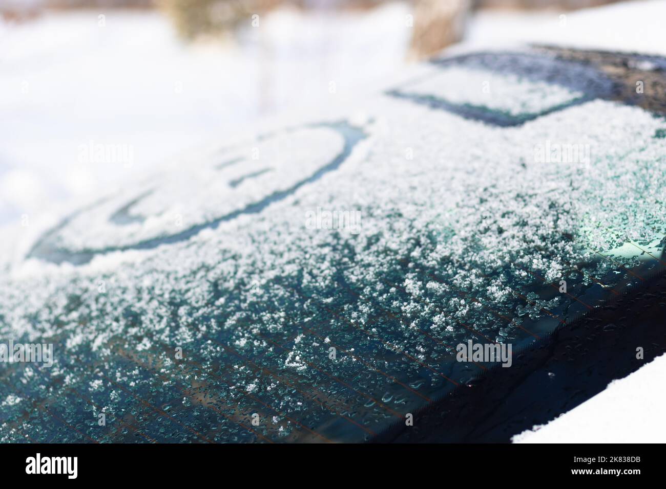 Zeichnung eines lächelnden Gesichts auf einem verschneiten Heckfenster eines Autos an einem sonnigen Wintertag. Selektiver Fokus. Nahaufnahme Stockfoto