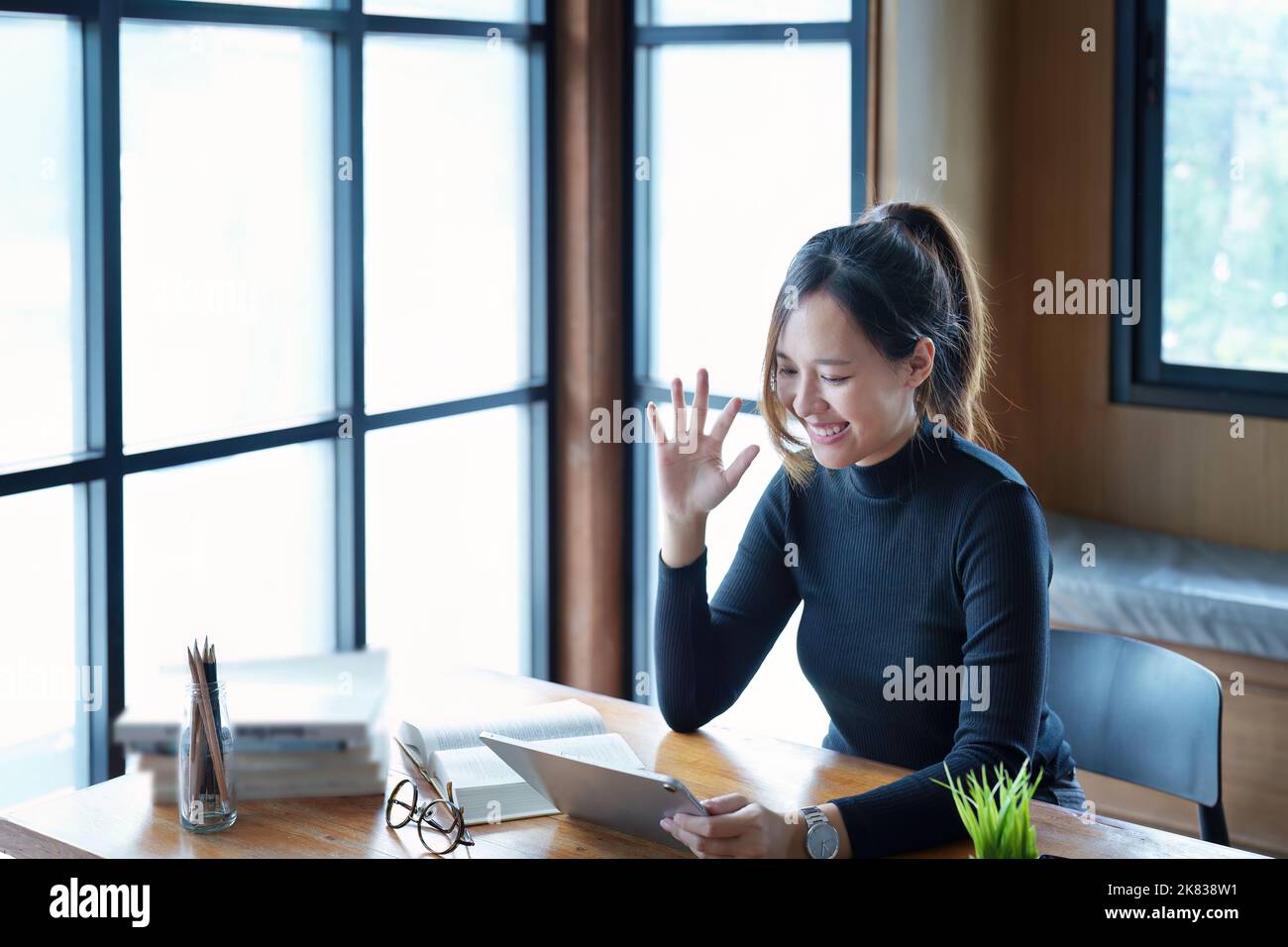 Porträt einer jungen asiatischen Frau, die mit einem Tablet-Computer und Büchern online über Videokonferenzen auf einem Holztisch in der Bibliothek studiert Stockfoto