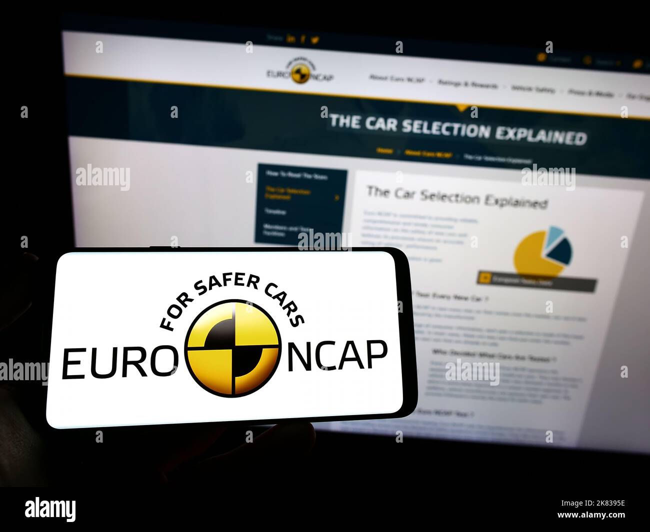 Person, die Mobiltelefon mit dem Logo des Sicherheitsprogramms Euro NCAP auf dem Bildschirm vor dem Logo hält. Konzentrieren Sie sich auf die Telefonanzeige. Stockfoto