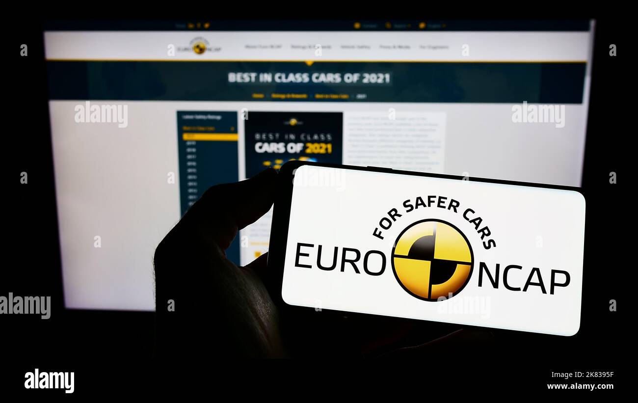 Person, die ein Mobiltelefon mit dem Logo des Sicherheitsprogramms Euro NCAP auf dem Bildschirm vor der Webseite hält. Konzentrieren Sie sich auf die Telefonanzeige. Stockfoto