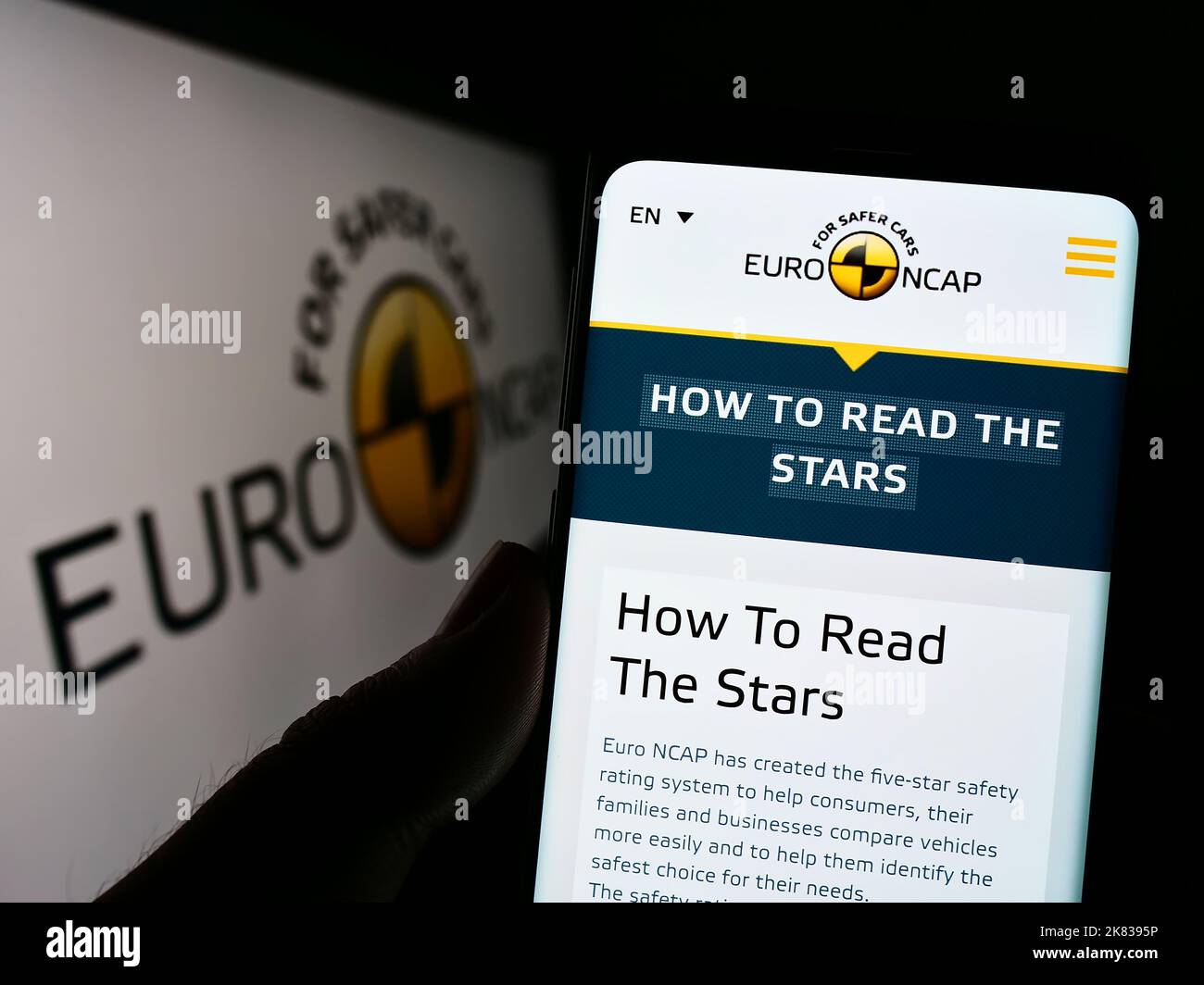 Person, die Mobiltelefon mit der Webseite des Sicherheitsprogramms Euro NCAP auf dem Bildschirm vor dem Logo hält. Konzentrieren Sie sich auf die Mitte des Telefondisplays. Stockfoto