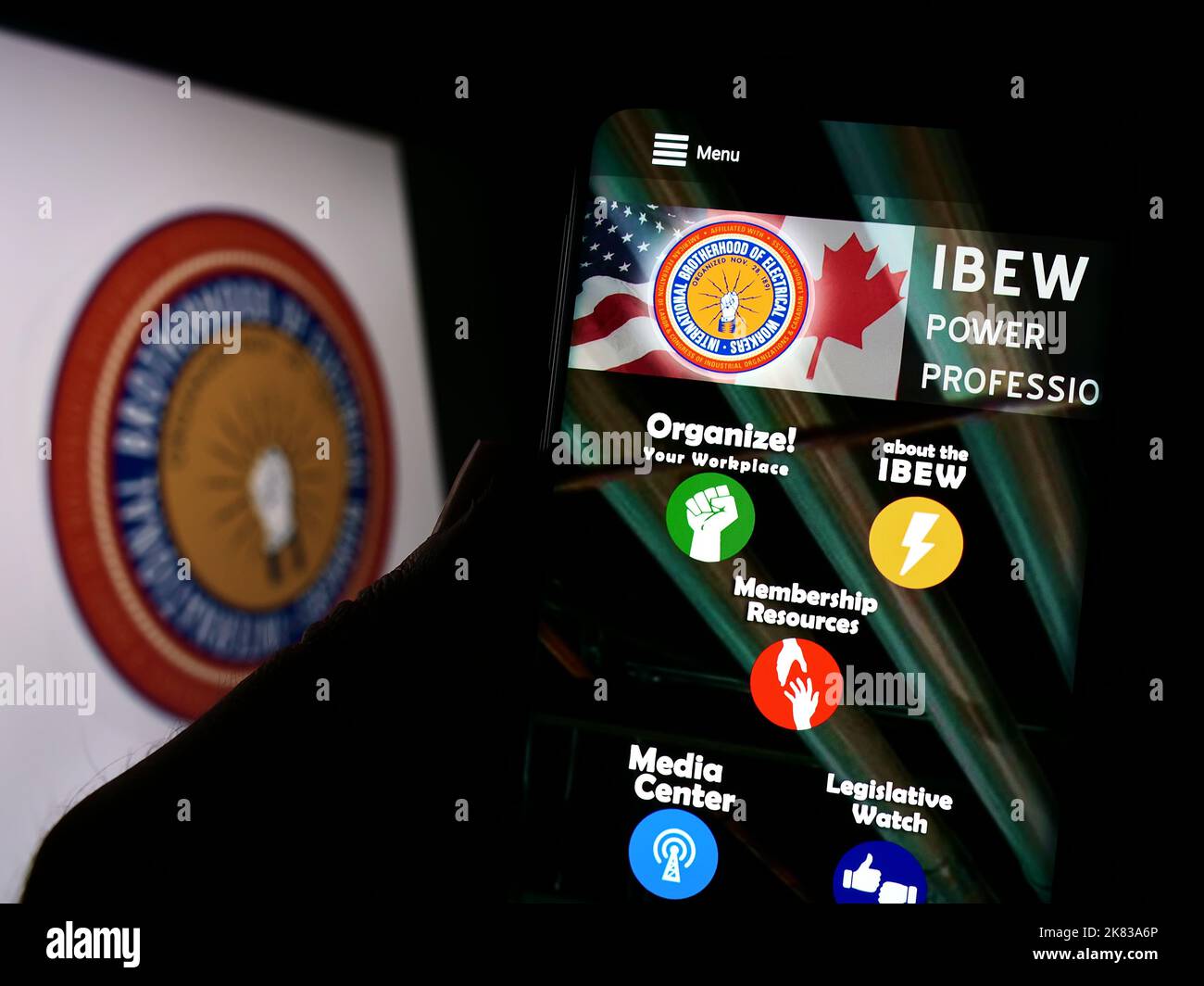 Person, die Mobiltelefon mit der Webseite der nordamerikanischen Gewerkschaft IBEW auf dem Bildschirm vor dem Logo hält. Konzentrieren Sie sich auf die Mitte des Telefondisplays. Stockfoto