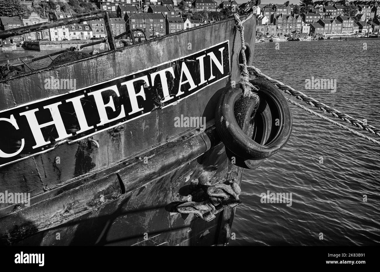 Das Bug eines verwitterten Fischerbootes liegt im Hafen. Ein Seil erstreckt sich bis zum Ufer und Gebäude säumten die gegenüberliegende Seite. Stockfoto