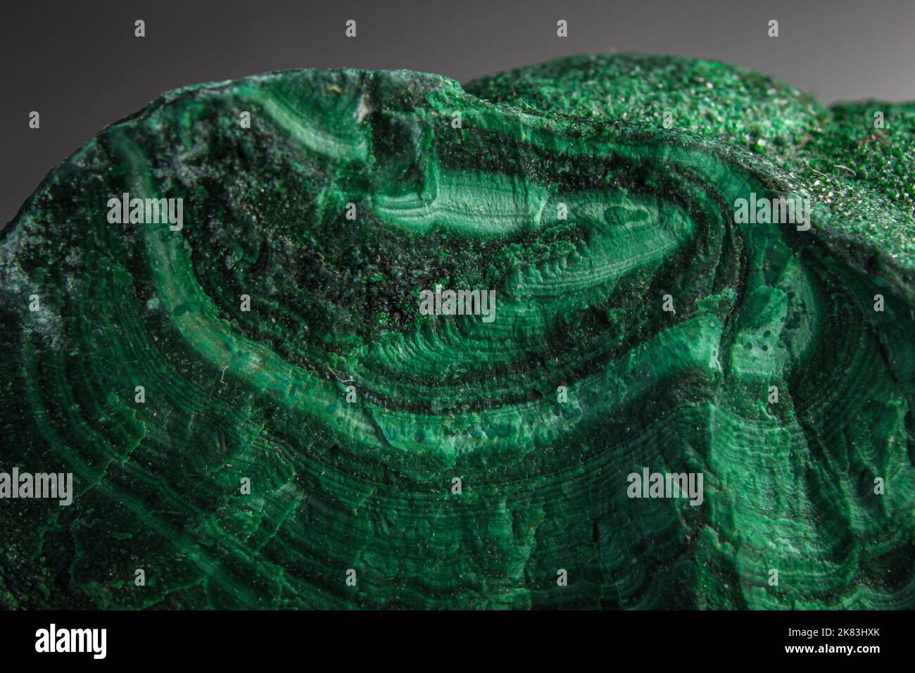 Malachit-Brocken-Stein auf der Silberoberfläche. Zufällig geformter grüner Stein mit Wellen und Grüntönen. Malachit ist ein grünes Kupfer Stockfoto