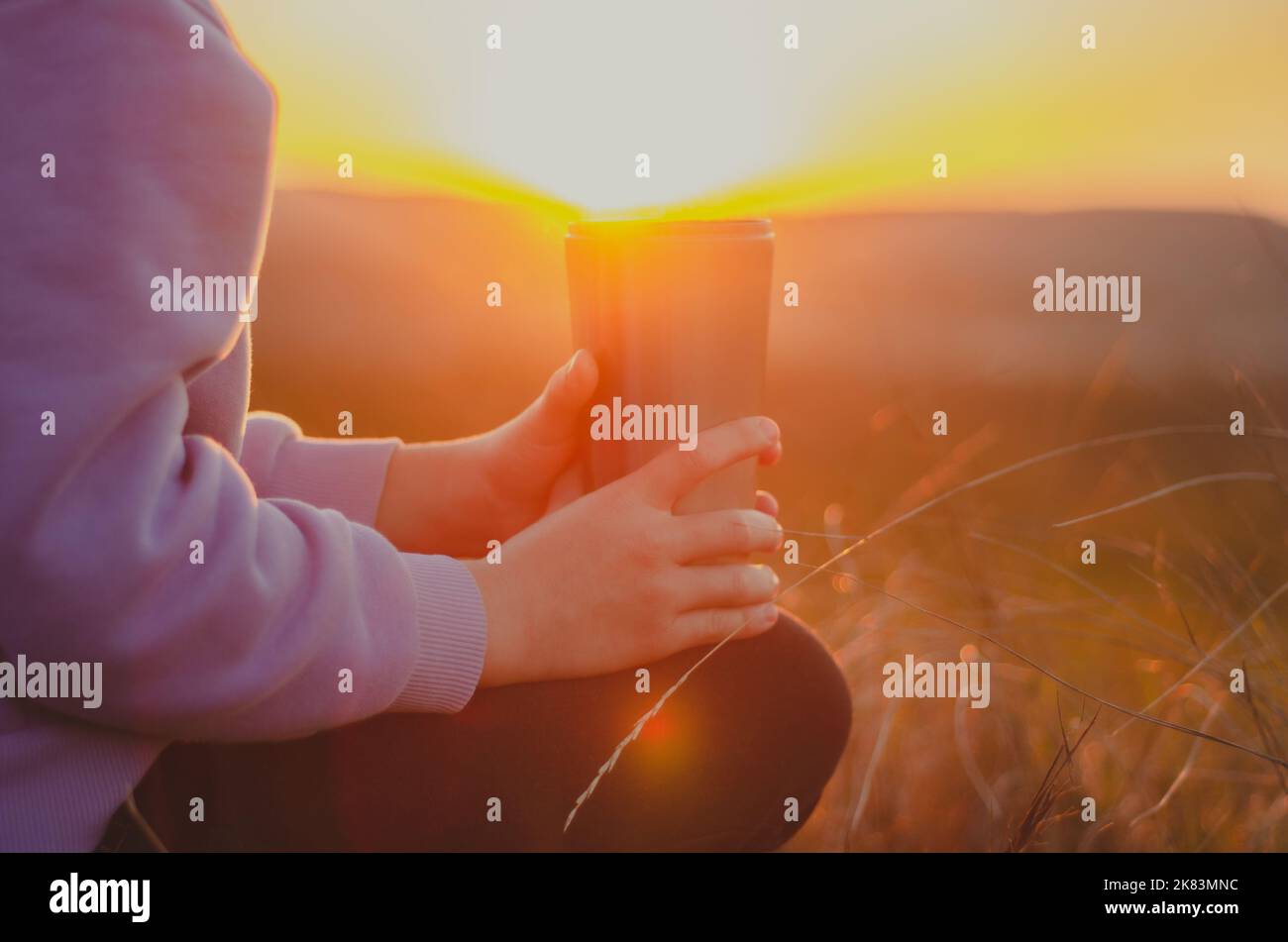 Person mit einer heißen Tasse Tee bei Sonnenuntergang Stockfoto